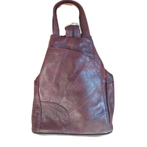 May include: A burgundy leather backpack with a top handle and adjustable straps. The bag features a patchwork design with visible stitching and a zippered closure. The backpack has a rounded shape and appears to be made of genuine leather.