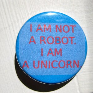 Könnte beinhalten: Ein blauer Knopf mit dem Text "Ich bin kein Roboter. Ich bin ein Einhorn." in roten Buchstaben.