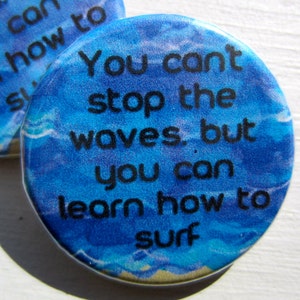 Op de afbeelding: Een blauwe en witte knop met de tekst "You can't stop the waves, but you can learn how to surf".