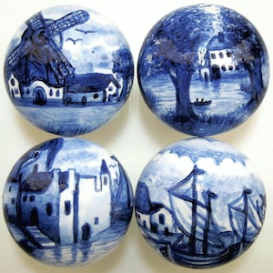 Pode incluir: Quatro ornamentos redondos de cerâmica com cenas pintadas em azul e branco no estilo Delft de paisagens holandesas. Os ornamentos apresentam um moinho de vento, uma casa à beira de um lago, um castelo e um veleiro.