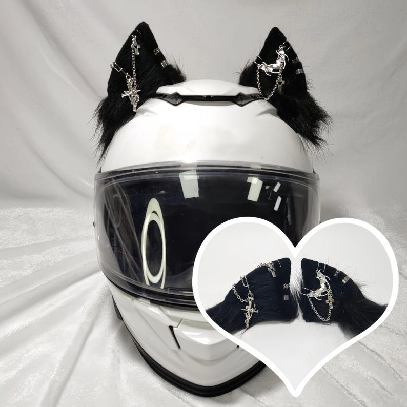 May include: White motorcycle helmet with black faux fur cat ears with silver chain and cross accents. The helmet has a clear visor.