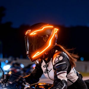 Può includere: Un casco da moto nero con luci a LED arancioni brillanti che delineano i bordi. Il casco ha una visiera scura. La persona indossa una giacca da moto bianca e nera. Lo sfondo è scuro con luci sfocate.