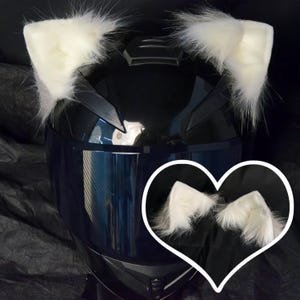 May include: White faux fur cat ears attached to a black motorcycle helmet. The ears are soft and fluffy, and they are a fun and stylish way to add a touch of personality to a helmet.