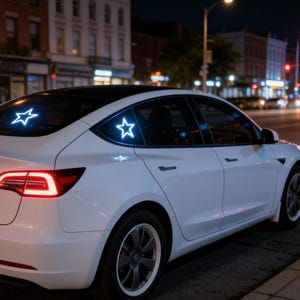 May include: White car with glowing star-shaped decals on the rear windows. The car is parked on a city street at night, with streetlights and buildings in the background. The car's rear lights are illuminated.