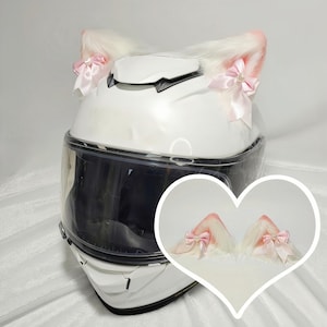 May include: White motorcycle helmet with a pair of white fuzzy cat ears with pink bows attached to the top.