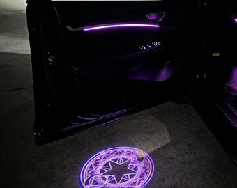 May include: A car door with purple interior lighting and a circular, illuminated design projected onto the ground. The design features a star and geometric shapes, with a purple glow.