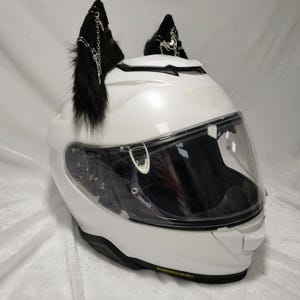 May include: White motorcycle helmet with a clear visor and black furry cat ears with silver chains and charms attached.