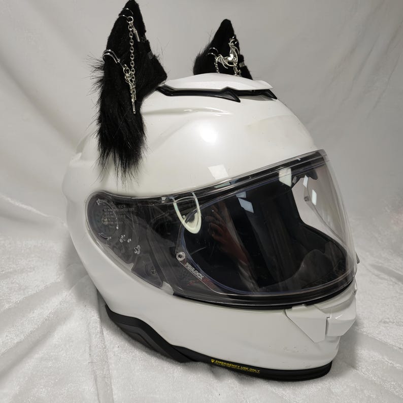 May include: White motorcycle helmet with a clear visor and black furry cat ears with silver chains and charms attached.
