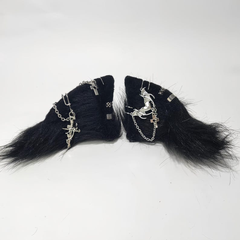 May include: A pair of black faux fur hair clips with silver chains, crosses, and a bat charm.