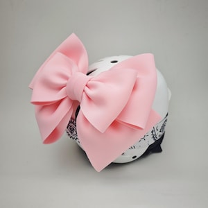 May include: A pink bow tied on a white helmet with a black and white bandana. The bow is large and fluffy.