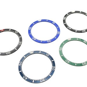 May include: Five watch bezels in different colors: black, blue, green, and two shades of gray. Each bezel has white numbers and markings.