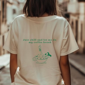 Könnte beinhalten: Cremefarbenes T-Shirt mit dem grünen Text "Just chill and let me do my coffee break". Darunter eine grüne Illustration einer Person, die sich in einer Kaffeetasse entspannt. Das T-Shirt wird von einer Person getragen.