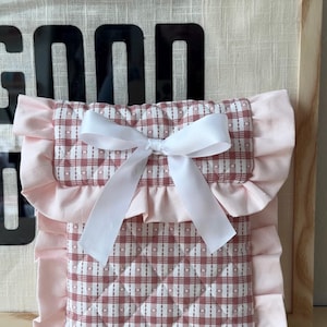 Puede incluir: Una bolsa de tela a cuadros rosa y blanca con un lazo de satén blanco y bordes con volantes.