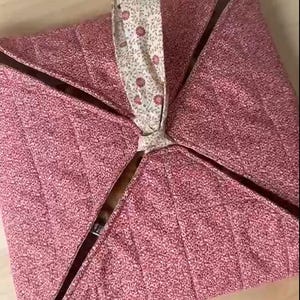 Könnte beinhalten: Ein rosa Stoffaufbewahrungskorb mit einem floralen Muster am Griff. Der Korb ist gesteppt und hat eine quadratische Form.