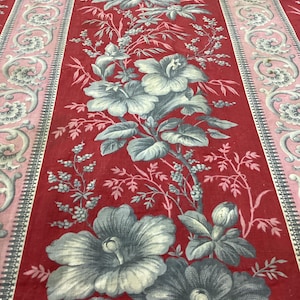 Pode incluir: Tecido vermelho com um padrão floral com grandes flores cinzentas e brancas. O design inclui um motivo floral central e bordas com um padrão de rolagem rosa e cinza. O tecido tem uma estética vintage.