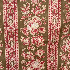 Könnte beinhalten: Nahaufnahme eines Stoffes mit einem sich wiederholenden Blumenmuster. Das Design zeigt rote und cremefarbene Blumen und Blätter auf braunem Hintergrund. Vertikale Streifen mit verzierten roten und cremefarbenen Designs umranden das Blumenmuster.