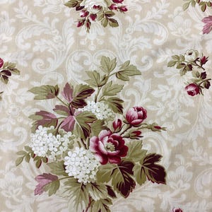 Könnte beinhalten: Blumenstoff mit cremefarbenem Hintergrund und einem sich wiederholenden Muster aus weißen, bordeauxroten und grünen Blumen und Blättern. Das Design umfasst Rosen und andere Blüten mit einer klassischen, Vintage-Ästhetik.