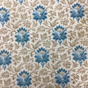 Può includere: Primo piano di un tessuto con un motivo floreale ripetuto. Il design presenta fiori blu stilizzati con centri color crema e viti e foglie marroni su sfondo crema. Il tessuto ha un'estetica vintage o antica.