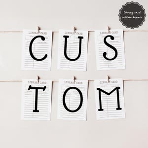 Può includere: Un banner con la scritta "CUSTOM" realizzato con repliche di schede di biblioteca, ogni lettera stampata in nero su sfondo bianco. Le schede sono sospese con mollette su uno spago. Un'etichetta circolare recita "library card custom banner".