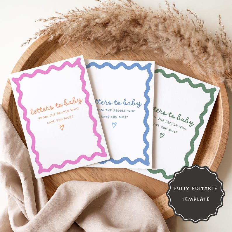 May include: Three white cards with pink, blue, and green scalloped borders. Each card has the text "letters to baby" and a heart symbol. The cards are displayed on a wooden tray, with dried plants in the background.