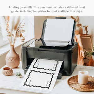 May include: A black printer with a white sheet of paper in the tray. The paper has a black border and text that reads "DEAR BABY, DATE:" and "WITH LOVE". The printer is on a white table with a candle and decorative items.