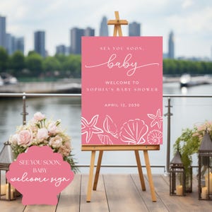 Könnte beinhalten: Ein rosa Willkommensschild für eine Babyparty auf einer Holzstaffelei. Auf dem Schild steht "Sea You Soon, Baby" und "Willkommen bei Sophias Babyparty, 12. April 2030." Weiße Muschelgrafiken verzieren den unteren Rand.