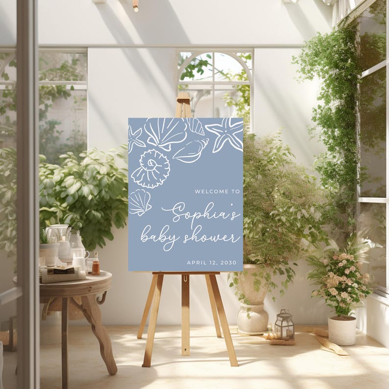 May include: A baby shower sign on a wooden easel. The sign is light blue with white seashell illustrations and text that reads "Welcome to Sophia's baby shower, April 12, 2030."