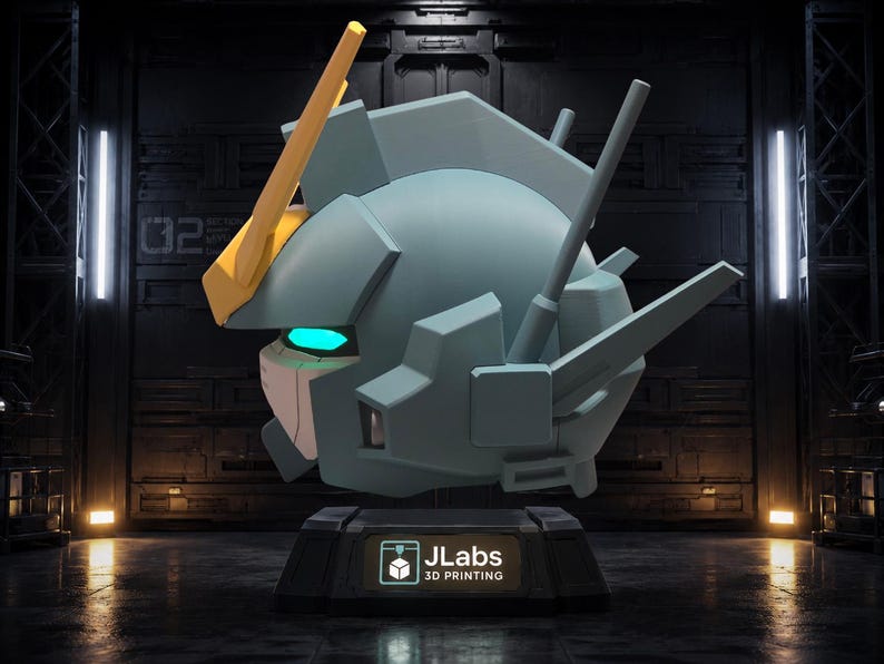 May include: A light blue robotic head sculpture featuring a prominent yellow V-fin antenna, glowing cyan eyes, and angular mechanical details. The head rests on a black pedestal base with a label that reads JLabs 3D PRINTING in white text.