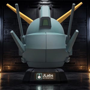 May include: A light blue robotic head sculpture with two yellow V-shaped antennae and multiple protruding sensors. The head rests on a black rectangular base featuring a logo with the text JLabs 3D PRINTING in white and teal lettering.