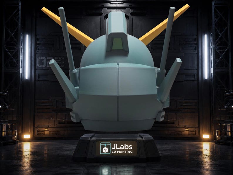 May include: A light blue robotic head sculpture with two yellow V-shaped antennae and multiple protruding sensors. The head rests on a black rectangular base featuring a logo with the text JLabs 3D PRINTING in white and teal lettering.