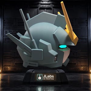 May include: A light blue robotic head sculpture featuring a yellow V-fin antenna, glowing cyan eyes, and angular mechanical details. The head is mounted on a black rectangular base with a label that reads JLabs 3D PRINTING in white text.