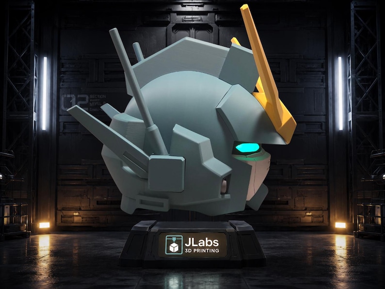 May include: A light blue robotic head sculpture featuring a yellow V-fin antenna, glowing cyan eyes, and angular mechanical details. The head is mounted on a black rectangular base with a label that reads JLabs 3D PRINTING in white text.