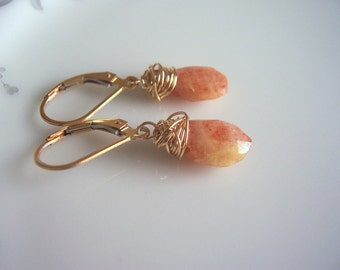Op de afbeelding: Gouden draad gewikkelde oorbellen met oranje sunstone edelstenen. De oorbellen hebben een traanvorm en zijn van een delicaat en elegant ontwerp.