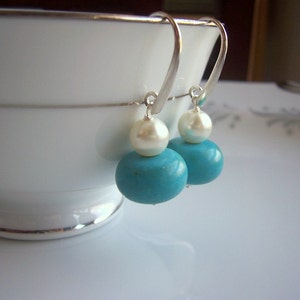 Op de afbeelding: Een paar zilveren oorhangers met turquoise en witte parels.