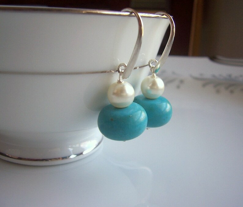Op de afbeelding: Een paar zilveren oorhangers met turquoise en witte parels.