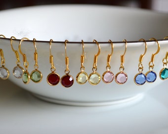 Op de afbeelding: Een set van 10 paar gouden oorhangers met ronde, kleurrijke edelstenen. De oorringen zijn verkrijgbaar in verschillende kleuren, waaronder helder, groen, rood, geel, roze, blauw en teal.