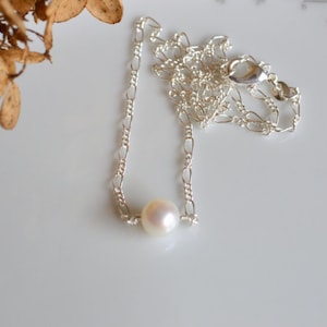 Pode incluir: Um delicado colar de corrente de prata com um &uacute;nico pingente de p&eacute;rola branca.