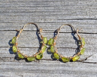 May include: A pair of gold hoop earrings with green gemstone accents. The earrings are made with wire wrapped around the stones.