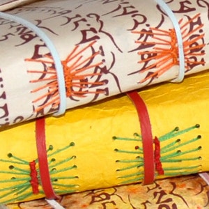 Puede incluir: Tres diarios hechos a mano con cubiertas de cuero y costuras decorativas. El diario superior tiene una cubierta crema con costuras marrones y naranjas. El diario del medio tiene una cubierta amarilla con costuras rojas y verdes. El diario inferior tiene una cubierta marr&oacute;n con costuras marrones.
