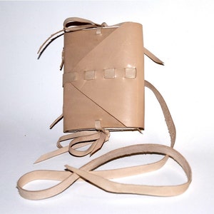 Può includere: Un diario in pelle marrone chiaro con una cinghia e una chiusura intrecciata. Il diario ha un design semplice ed è realizzato in pelle naturale.