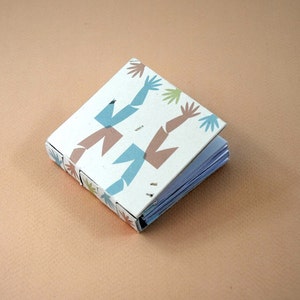 May include: A small, white book with a colorful pattern of blue, brown, and green abstract shapes. The book is bound with a white thread and has a white cover.