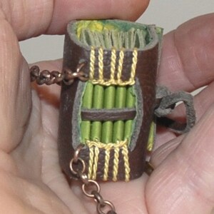 May include: A small, brown leather-bound journal with a green and yellow patterned cover. The journal is attached to a brown chain.