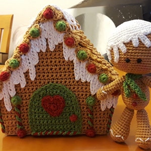 May include: A crocheted gingerbread house with white icing and red and green candy decorations. A crocheted gingerbread person stands next to the house.
