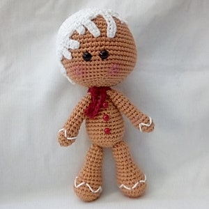 May include: A crocheted gingerbread man toy with white icing details, red buttons, and a red scarf.