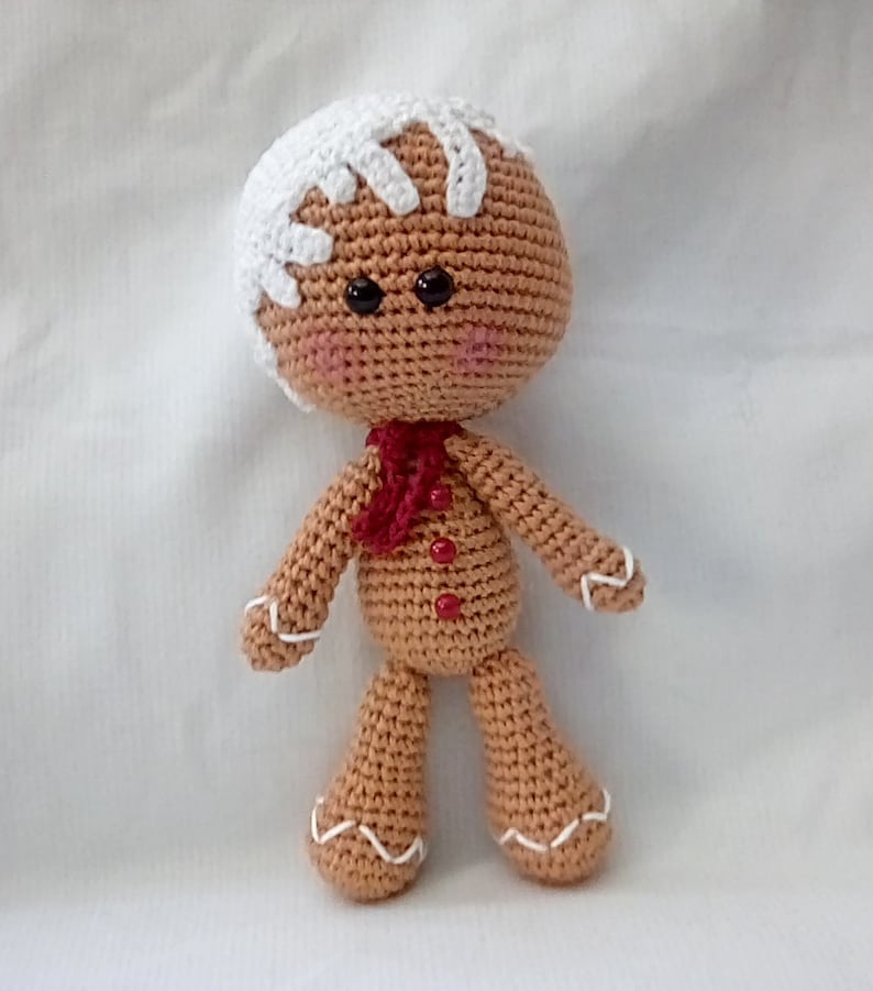 May include: A crocheted gingerbread man toy with white icing details, red buttons, and a red scarf.