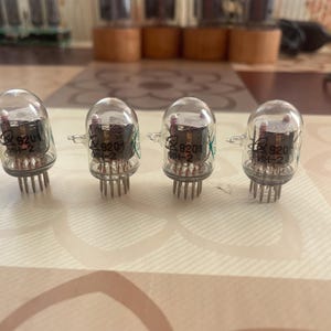 May include: Four clear glass vacuum tubes with visible internal components and metal pins. Each tube has the markings "9201" and "ИН-2". The tubes are arranged in a row on a patterned surface, with other tubes visible in the background.