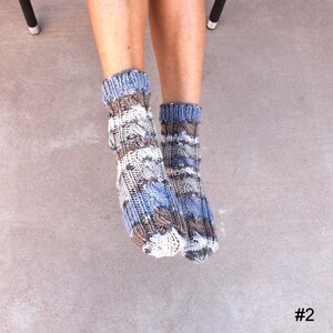May include: A pair of cable-knit socks in shades of blue, brown, and white. The socks have a textured pattern and are worn on a person's feet. The socks are a cozy and warm accessory.