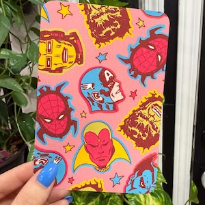 May include: A rectangular card with a pink background featuring a repeating pattern of comic book character heads including Spider-Man, Captain America, Vision, and Iron Man, interspersed with small blue and yellow stars throughout the design.