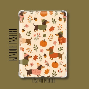 May include: A rectangular Kindle insert featuring a repeating pattern of brown dachshunds wearing sweaters and hats, interspersed with orange pumpkins, acorns, and autumn leaves on a cream background. The text reads KINDLE INSERT and CASE NOT INCLUDED.