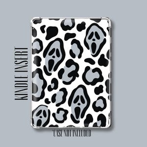 May include: A rectangular Kindle insert featuring a repeating pattern of black and grey ghost-like masks against a white background. The text "KINDLE INSERT" is printed on the left side, and "CASE NOT INCLUDED" is printed at the bottom.